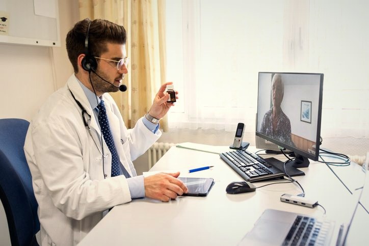 A clinician on a telehealth call, holding a medication for a remote patient